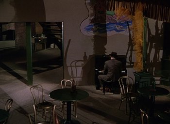 Movie still from “Cover Girl” (1944), directed by Charles Vidor – A man in a suit and hat playing a piano in a restaurant; Wide shot, High angle