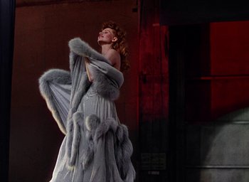 Movie still from “Cover Girl” (1944), directed by Charles Vidor – A woman in a long gray dress holding a fur coat; Medium shot, Low angle