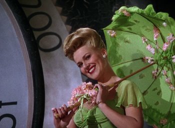 Movie still from “Cover Girl” (1944), directed by Charles Vidor – A woman holding an umbrella and wearing a green dress; Medium shot, Low angle