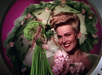 Movie still from “Cover Girl” (1944), directed by Charles Vidor – A woman holding an open umbrella in front of a picture of herself; Medium shot, Low angle