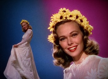 Movie still from “Cover Girl” (1944), directed by Charles Vidor – A woman in a white dress and a woman in a yellow flower crown; Medium shot, Low angle