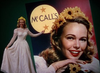 Movie still from “Cover Girl” (1944), directed by Charles Vidor – A woman in a white dress standing in front of an advertisement; Medium shot, Low angle