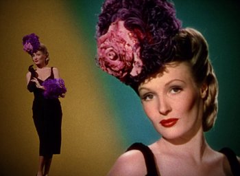 Movie still from “Cover Girl” (1944), directed by Charles Vidor – A woman in a black dress with a purple hat on her head; Medium shot, Low angle