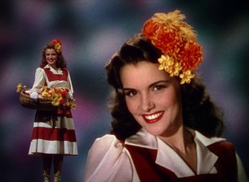 Movie still from “Cover Girl” (1944), directed by Charles Vidor – A woman in a red and white striped dress holding a basket of flowers; Medium shot, Low angle