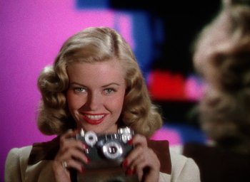 Movie still from “Cover Girl” (1944), directed by Charles Vidor – A woman is holding a camera and smiling for the camera; Close Up shot, Low angle