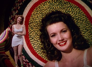 Movie still from “Cover Girl” (1944), directed by Charles Vidor – A woman in a white dress standing next to another woman in a white dress; Medium shot, Low angle