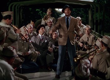 Movie still from “Cover Girl” (1944), directed by Charles Vidor – A group of men sitting around a man in a suit and tie; Wide shot, High angle