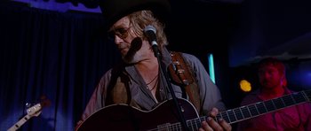 Movie still from “Crazy Heart” (2009), directed by Scott Cooper – A man with a hat and glasses playing a guitar; Medium shot, Low angle