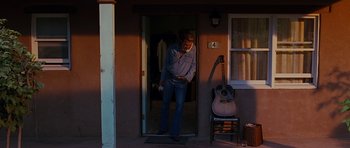 Movie still from “Crazy Heart” (2009), directed by Scott Cooper – A man standing in front of an open door with a guitar; Wide shot, Over the shoulder angle