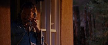 Movie still from “Crazy Heart” (2009), directed by Scott Cooper – A person standing in front of a building holding a cell phone; Medium shot, Over the shoulder angle