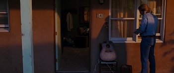 Movie still from “Crazy Heart” (2009), directed by Scott Cooper – A guitar sitting on top of a chair in a room; Wide shot, High angle