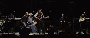 Movie still from “Crazy Heart” (2009), directed by Scott Cooper – A group of people on a stage with a man playing a guitar; Wide shot, Over the shoulder angle