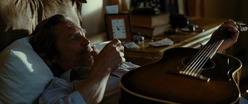 Movie still from “Crazy Heart” (2009), directed by Scott Cooper – A man sitting in front of a guitar in a room; Medium shot, High angle
