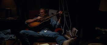 Movie still from “Crazy Heart” (2009), directed by Scott Cooper – A man sitting on a couch playing a guitar; Medium shot, Low angle