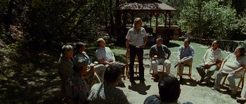 Movie still from “Crazy Heart” (2009), directed by Scott Cooper – A group of people sitting in a circle with a man standing in front of them; Wide shot, Over the shoulder angle
