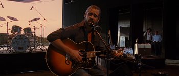 Movie still from “Crazy Heart” (2009), directed by Scott Cooper – A man sitting in front of a microphone playing an acoustic guitar; Medium shot, Low angle