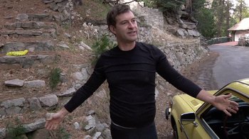 Movie still from “Creep” (2014), directed by Patrick Brice – A man standing next to a car on a rocky hillside; Medium shot, Low angle