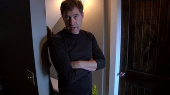Movie still from “Creep” (2014), directed by Patrick Brice – A man standing in front of a door with his arms crossed; Medium shot, Low angle