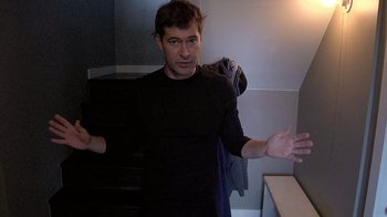 Movie still from “Creep” (2014), directed by Patrick Brice – A man standing in a room with his arms outstreched; Medium shot, Low angle