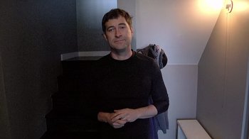 Movie still from “Creep” (2014), directed by Patrick Brice – A man in a black shirt is standing in front of a mirror; Medium shot, Low angle