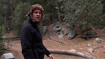 Movie still from “Creep” (2014), directed by Patrick Brice – A man wearing a fur hat standing next to a fallen tree; Medium shot, Over the shoulder angle