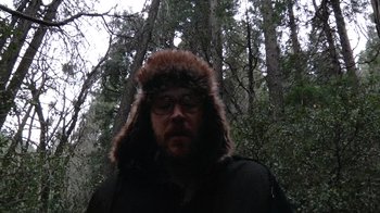 Movie still from “Creep” (2014), directed by Patrick Brice – A man in a fur hat standing in front of a forest; Close Up shot, Low angle