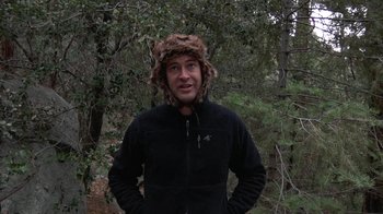 Movie still from “Creep” (2014), directed by Patrick Brice – A man wearing a hat standing in a wooded area; Medium shot, Over the shoulder angle