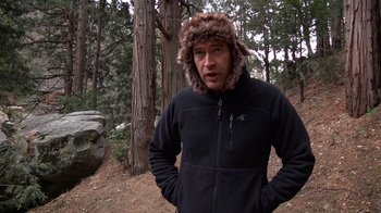Movie still from “Creep” (2014), directed by Patrick Brice – A man wearing a fur hat standing in the woods; Medium shot, Over the shoulder angle