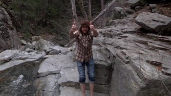 Movie still from “Creep” (2014), directed by Patrick Brice – A man in a plaid shirt is standing on a rocky path; Wide shot, High angle