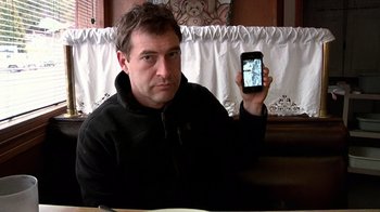Movie still from “Creep” (2014), directed by Patrick Brice – A man holding up a cell phone in his hand; Close Up shot, Over the shoulder angle