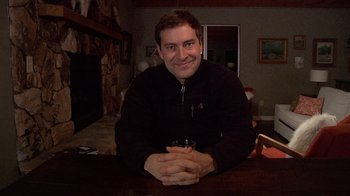 Movie still from “Creep” (2014), directed by Patrick Brice – A man sitting at a table with a drink in his hand; Medium shot, Low angle