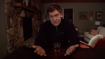 Movie still from “Creep” (2014), directed by Patrick Brice – A man sitting at a table with a glass of whiskey; Medium shot, Low angle