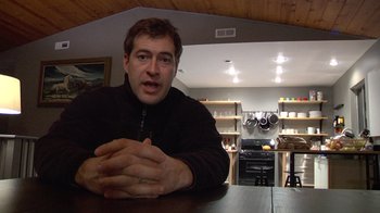 Movie still from “Creep” (2014), directed by Patrick Brice – A man sitting at a table in front of a stove; Medium shot, Low angle