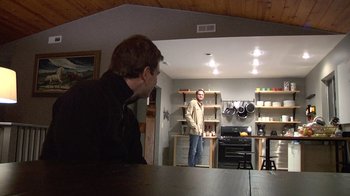 Movie still from “Creep” (2014), directed by Patrick Brice – A man standing in front of another man in a kitchen; Wide shot, Over the shoulder angle