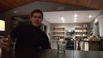 Movie still from “Creep” (2014), directed by Patrick Brice – A man sitting at a table with a glass of water in front of him; Medium shot, Low angle