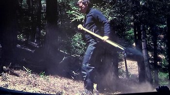 Movie still from “Creep” (2014), directed by Patrick Brice – A man holding a baseball bat while standing in the woods; Wide shot, Low angle