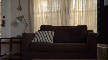 Movie still from “Creep” (2014), directed by Patrick Brice – A brown couch with a striped pillow on top of it; Wide shot, Low angle