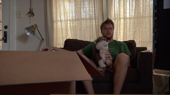 Movie still from “Creep” (2014), directed by Patrick Brice – A man sitting on a couch holding a stuffed animal; Medium shot, High angle