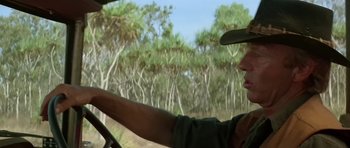 A man driving a car on a dirt road near a forest