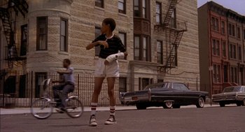 Movie still from “Crooklyn” (1994), directed by Spike Lee – A young boy is standing on the sidewalk holding a water bottle; Wide shot, Low angle