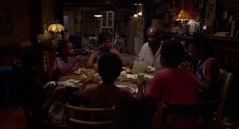 Movie still from “Crooklyn” (1994), directed by Spike Lee – A group of people sitting around a table eating food; Wide shot, High angle