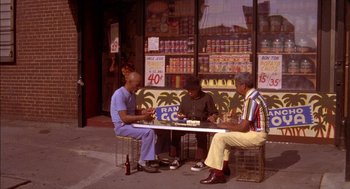 Movie still from “Crooklyn” (1994), directed by Spike Lee – Three people sitting at a table outside a store; Wide shot, High angle