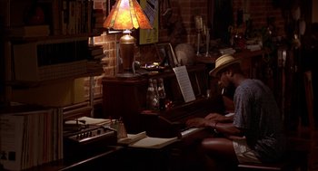 Movie still from “Crooklyn” (1994), directed by Spike Lee – A man sitting at a table playing a piano; Wide shot, High angle
