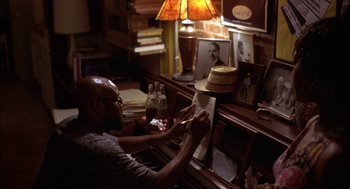 Movie still from “Crooklyn” (1994), directed by Spike Lee – A man sitting in front of a piano in a room; Medium shot, High angle