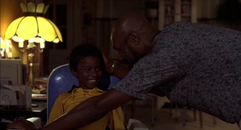 Movie still from “Crooklyn” (1994), directed by Spike Lee – An older man is giving a young boy a haircut; Medium shot, Over the shoulder angle
