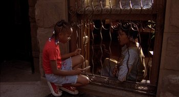 Movie still from “Crooklyn” (1994), directed by Spike Lee – Two young girls sitting on the ground looking at a cell phone; Medium shot, High angle