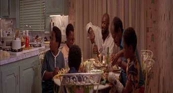 Movie still from “Crooklyn” (1994), directed by Spike Lee – A group of people sitting around a table eating food; Medium shot, High angle