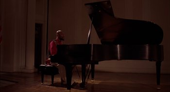 Movie still from “Crooklyn” (1994), directed by Spike Lee – A man sitting in front of a grand piano in a room; Medium shot, High angle