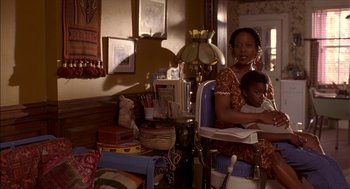 Movie still from “Crooklyn” (1994), directed by Spike Lee – A woman sitting in a chair holding a baby; Medium shot, High angle