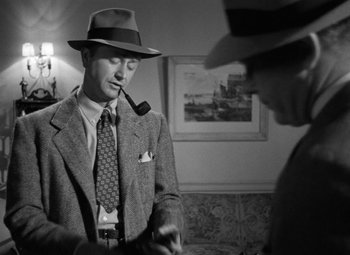 Movie still from “Crossfire” (1947), directed by Edward Dmytryk – A man smoking a pipe while standing next to another man in a suit; Close Up shot, Low angle